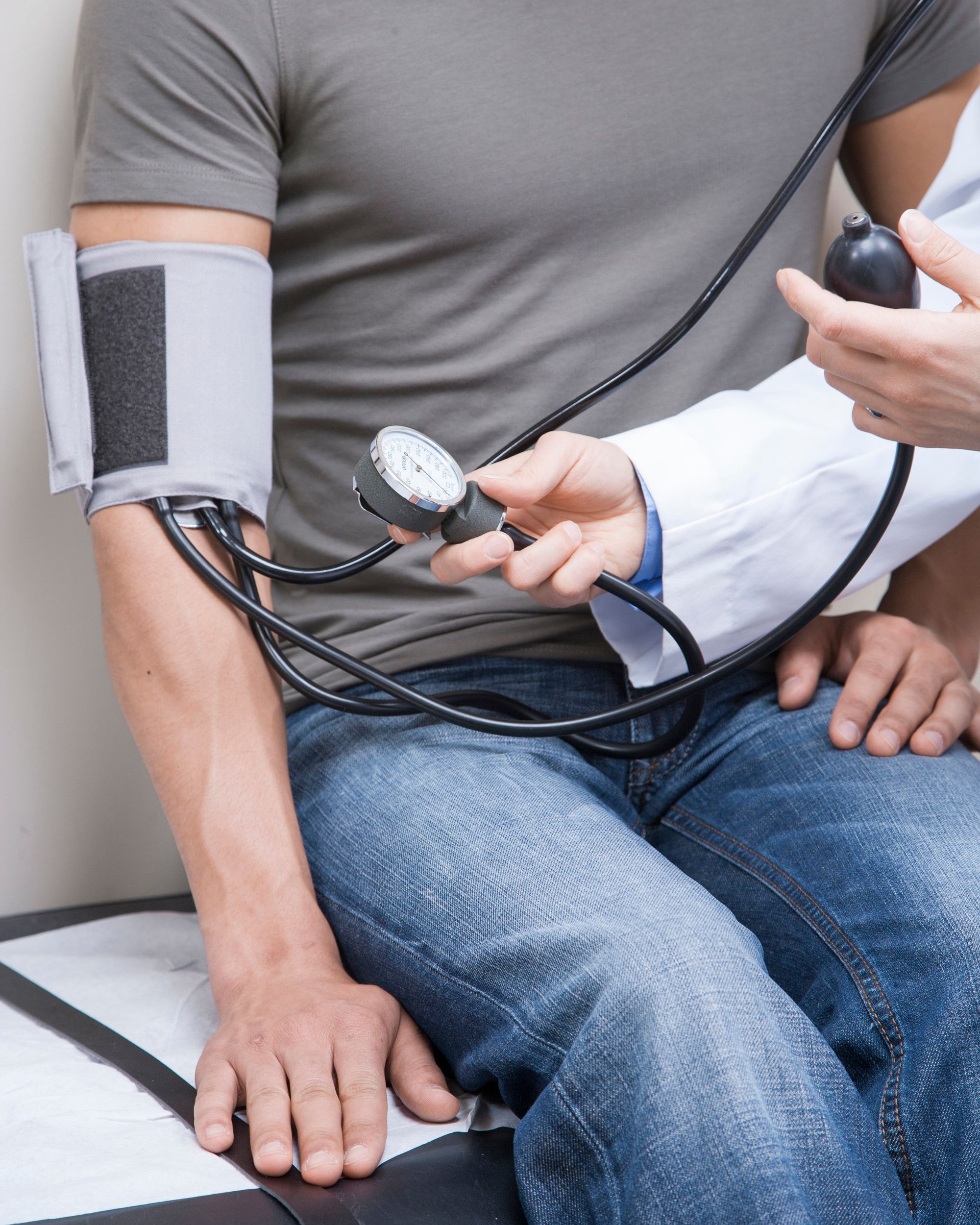 A clinician checks a seated patient's blood pressure with a manual cuff and gauge during a routine office visit.
